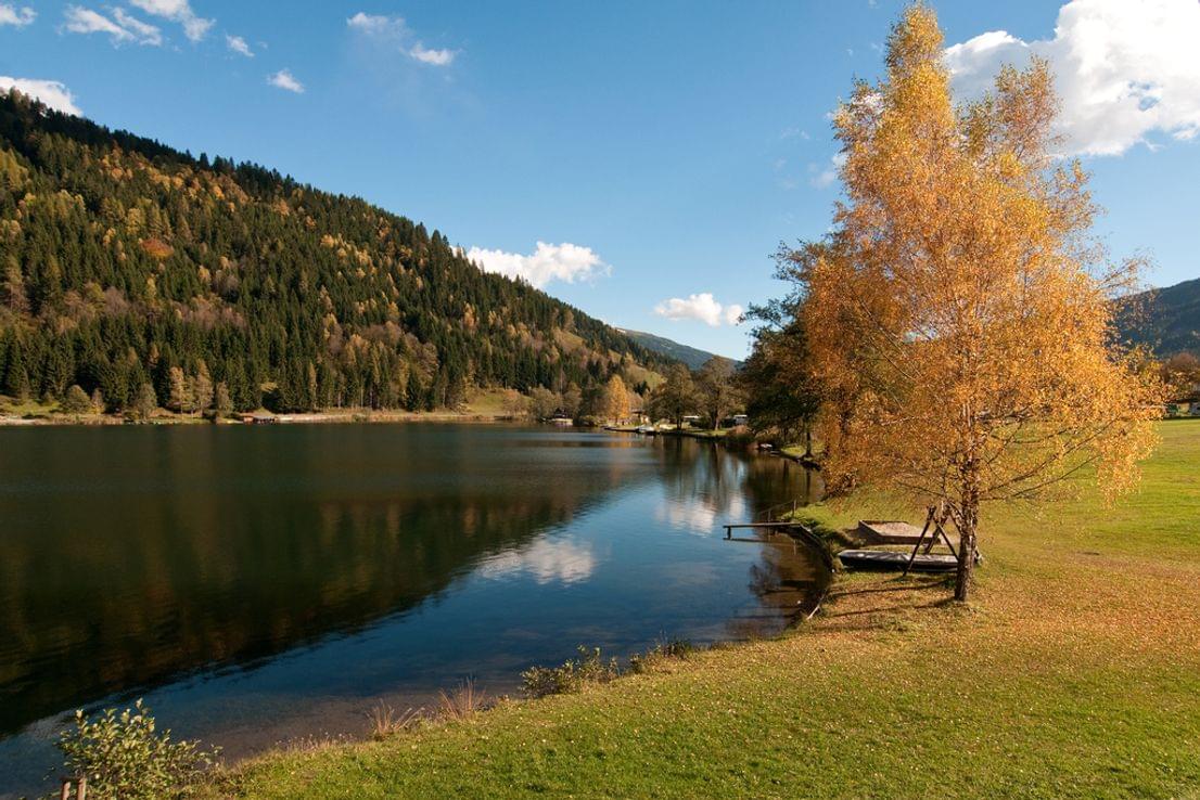 Herbstbäume an einem ruhigen Bergsee mit klarem Himmel und bewaldeten Hügeln